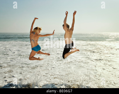 Couple leaping into waves on beach Stock Photo