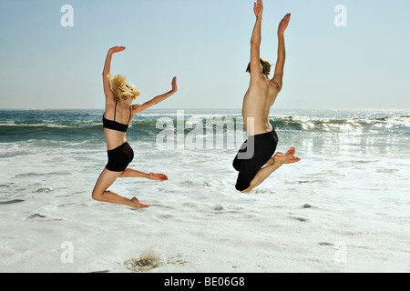 Couple leaping into waves on beach Stock Photo