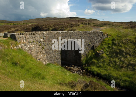 Old drystone bridge with one arch in the hills of the Isle of Skye called the fairy bridge with menacing cloud behind it Stock Photo