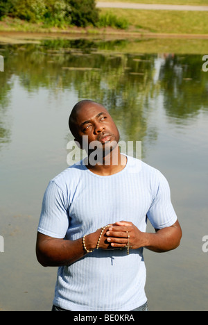 Young black man holding rosary looking thoughtful by pond Stock Photo