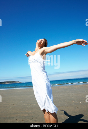 A woman standing on the beach with eyes closed and arms outstretched Stock Photo