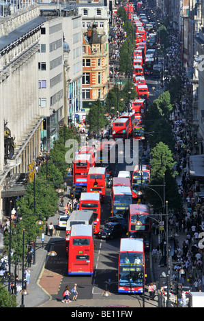 Looking down on busy UK Oxford Street with shoppers &aerial views of long queues of double decker red London buses waiting at bus stop & junctions Stock Photo