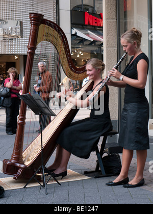 Two young female musicians playing harp and clarinet busking in pedestrian street in central Cologne Germany Stock Photo