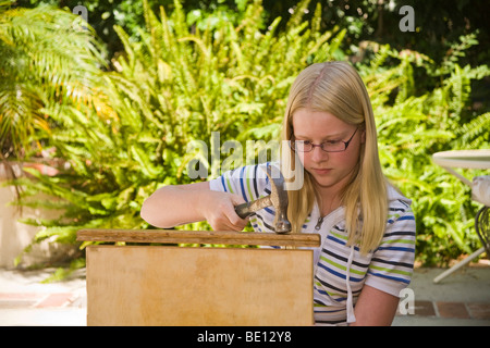 young person people 11-13 year old repairing cutting board by hammering nail back into wooden cutting board.  MR Myrleen Pearson Stock Photo
