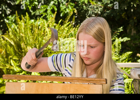 young person people  Tween tweens Young girl 11-13 year old repairing cutting board by hammering nail back into wooden cutting board MR Myrleen Pearson Stock Photo