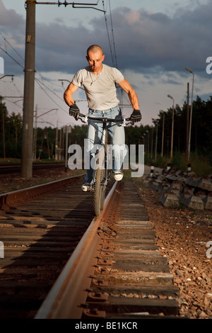Young man riding with bicycle on railways rail. Stock Photo
