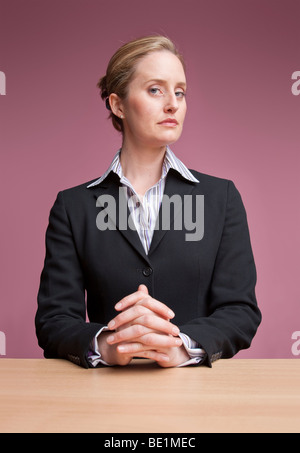 Female presenter sitting at desk with hands clasped Stock Photo