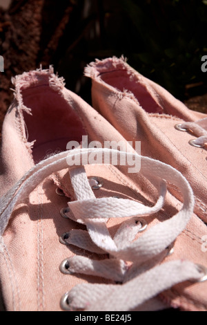 pair of old worn pink sneakers with white laces on a green background ...
