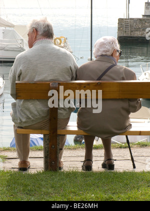 Two elderly people sat on a bench looking out to a lake Stock Photo