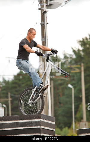 Young man standing on concrete blocks without front wheel in urban area with railways in background. Low angle view. Stock Photo