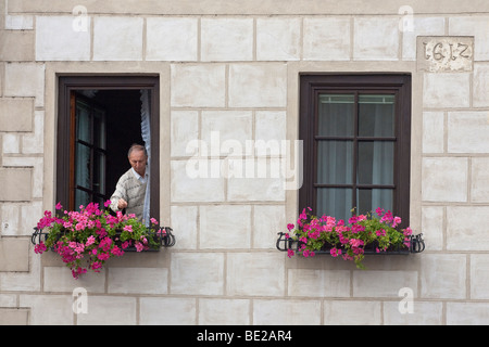 A man tends his flowers in window boxes in Krems, Austria. A stone indicates his house was built originally in 1612. Stock Photo