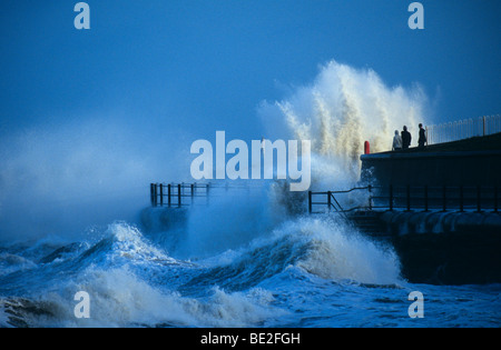 Waves breaking over sea defences watched by teenagers Stock Photo