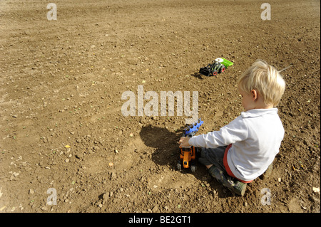 Child blond boy playing Plastic Toy Tractor on field Stock Photo