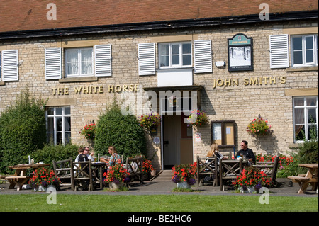 People enjoying drinks and lunch outside a pub called the white horse in England in summer. Stock Photo