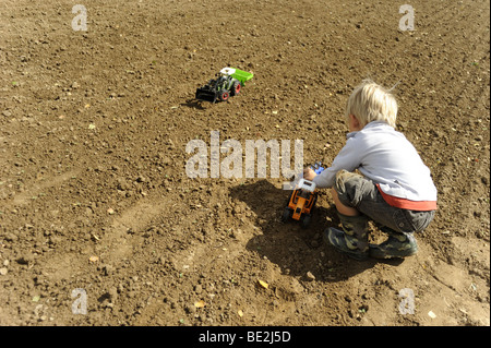 Child blond boy playing Plastic Toy Tractor on field Stock Photo