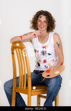 Artist sitting on a chair, holding a brush and colour palette, laughing Stock Photo