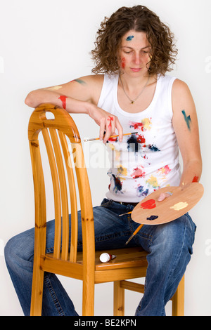 Artist sitting on a chair, holding a brush and colour palette, pensive Stock Photo