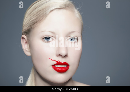 Portrait of a young blond woman with lipstick bleeding above her lip looking towards the viewer, imperfect, beauty Stock Photo