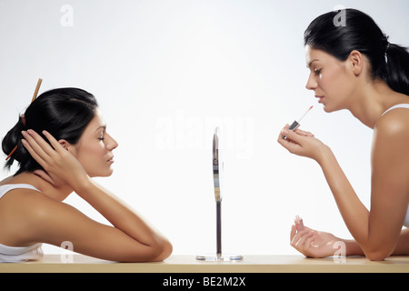 Two young women applying makeup sitting opposite one another, beauty Stock Photo