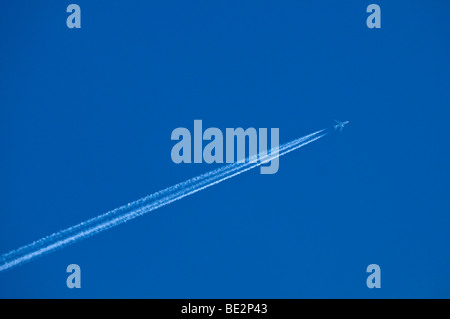 Airplane with multiple contrails in the blue sky Stock Photo