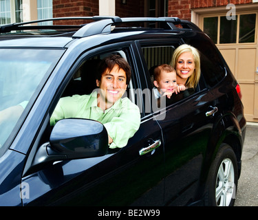 Happy young family sitting in black car looking out windows Stock Photo