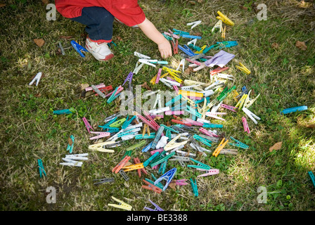 looking down at scattered multi coloured clothes pegs on grass lawn being picked up by partly cropped young child Stock Photo