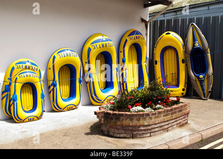 a row of different sized yellow inflatable dinghies up for sale lined up behind brick boat flower bed outside shop in tourist spot Stock Photo