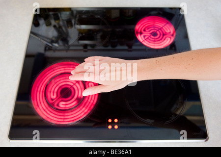 Household accident, girl touching glowing hotplate Stock Photo