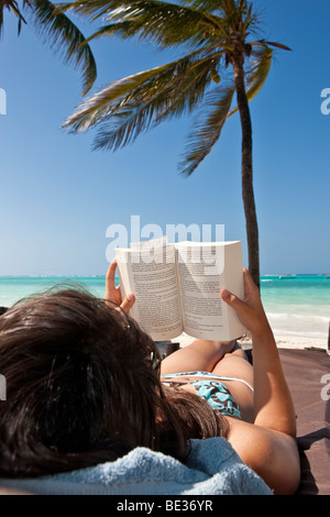Young woman on a beach reading a book under palm trees Stock Photo