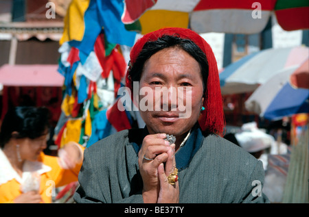 Tibetan man from the Kampha tribe with red hair knot, holding the symbol of the Tibetan snow lion as a trouser button with both Stock Photo