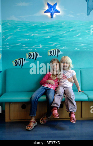 Two girls, sisters, on a bench in front of a painted wall Stock Photo
