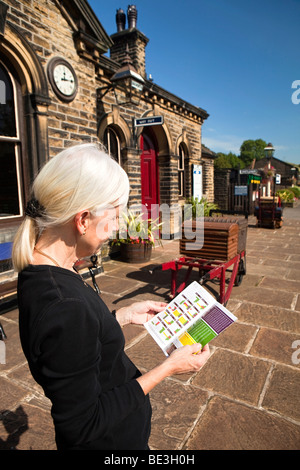 UK, England, Yorkshire, Keighley and Worth Valley Railway, woman waiting on Oakworth Station platform looking at train timetable Stock Photo