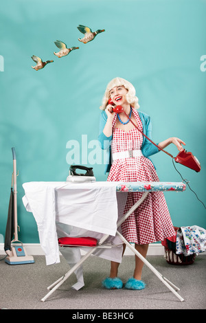 Retro image of 1960s housewife talking on the telephone whilst ironing Stock Photo