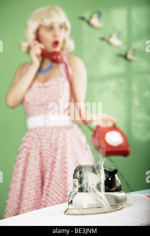 Retro housewife on telephone, with iron burning a shirt in the foreground. Stock Photo