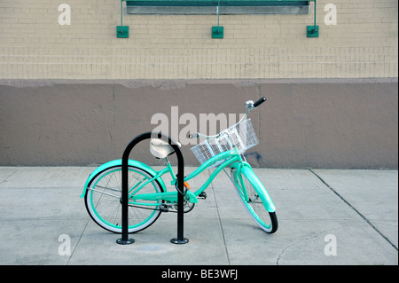 A women's turquoise green open frame Beach Cruiser style bicycle with a basket on the handlebars, locked to a bicycle stand in New York City Stock Photo