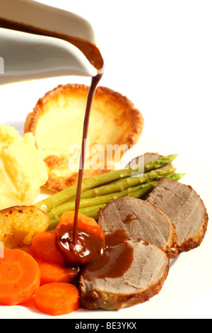 A meal of roast beef with carrots, Yorkshire puddings, potatoes and asparagus, with gravy being poured on Stock Photo
