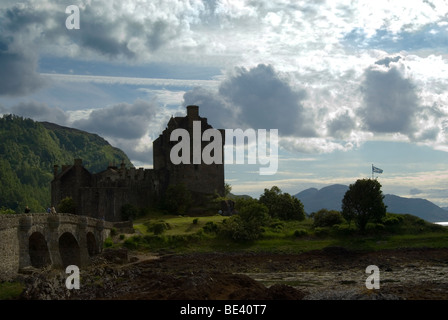 Eilean Donan castle backlit on a fine day with some clouds the bridge to the castle on the left and the flag of Scotland flying Stock Photo