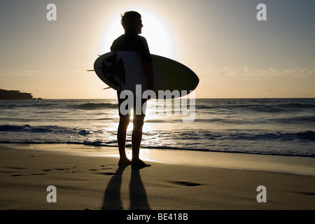 A surfer carrying surfboard is silhouetted by the morning sun.  Bondi Beach. Sydney, New South Wales, AUSTRALIA Stock Photo