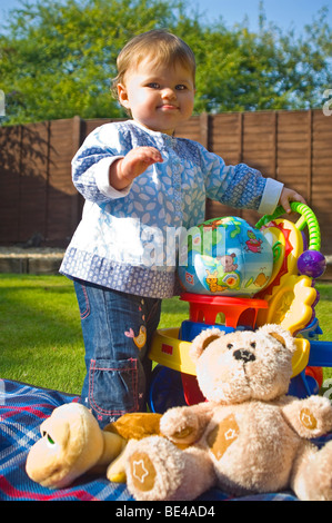 Vertical portrait of a young baby girl looking happy with herself as she stands up on her own in the garden. Stock Photo