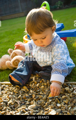 Vertical portrait of a young baby girl exploring her surroundings outside in the garden. Stock Photo