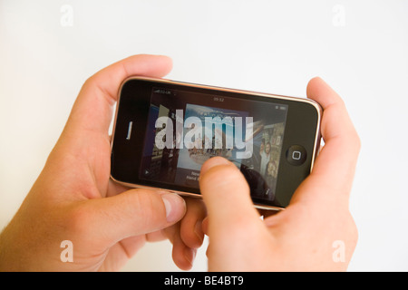 Man's hand holding an Apple iphone mobile cell phone viewing itunes albums horizontally. England UK Britain Stock Photo