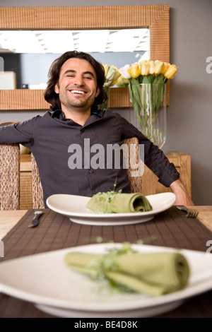 Young man sitting at the dining table, beaming Stock Photo