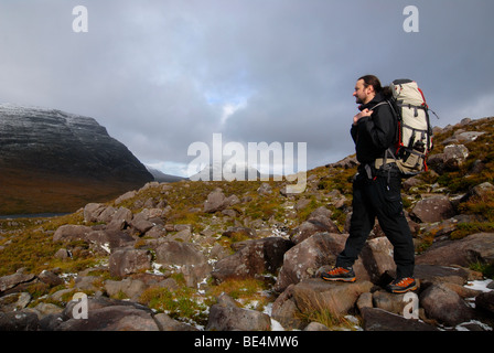 Hiker with hiking backpack on mountain trail in front of a snowy peak, Liathach, Torridon, Scotland, United Kingdom, Europe Stock Photo