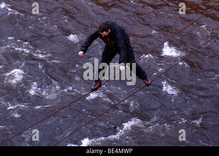 Adventurous hiker crossing over the wire ropes of a drawbridge, rope bridge in Glen Etive, Scotland, United Kingdom, Europe Stock Photo