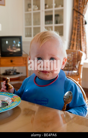 Young boy at the breakfast table holding a spoon and a piece of toast. Stock Photo
