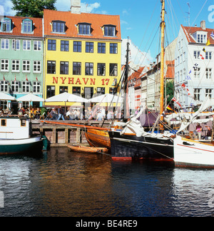 A sunny view of the harbour buildings, tourists people relaxing and boats along Nyhavn Harbor in the European city of Copenhagen Denmark Europe EU Stock Photo