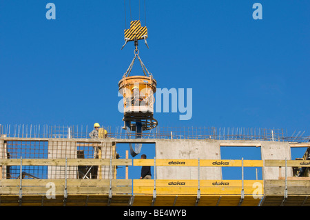 Pouring concrete on a building site with a concrete bucket and hose, construction workers on site, rebar exposed at the top of  Stock Photo