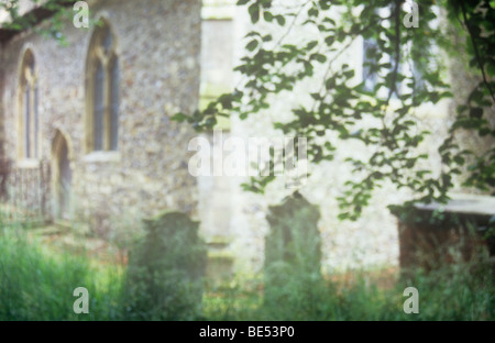 Impressionistic view of archetypal English church with gravestones in front framed by long green grass and leaves of Beech tree Stock Photo