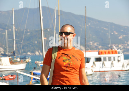 young man smiling while walking along some ships in an harbour Stock Photo
