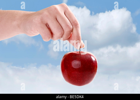 Hand holding a red apple against a blue sky Stock Photo